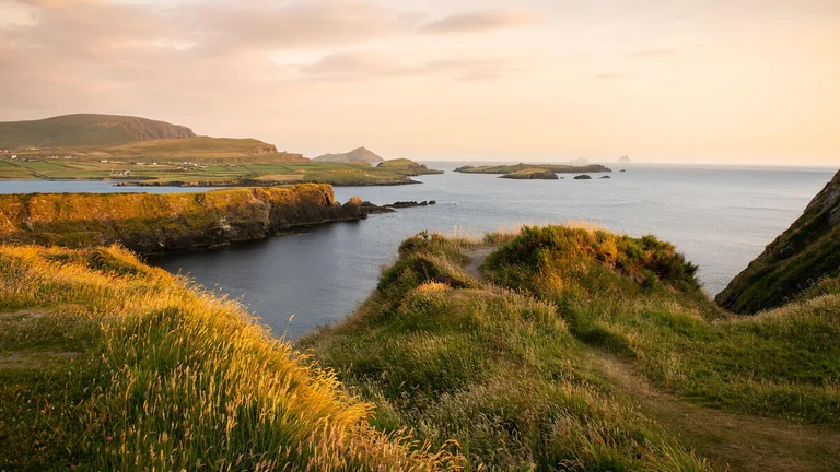 A grassy hill with a body of water and land in the background
