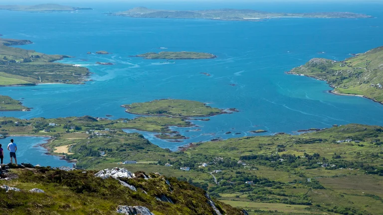 two people standing on a cliff overlooking multiple islands and coast