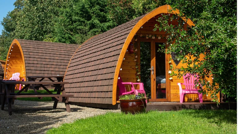 Two wooden cabins with curved roofs and picnic benches outside them.