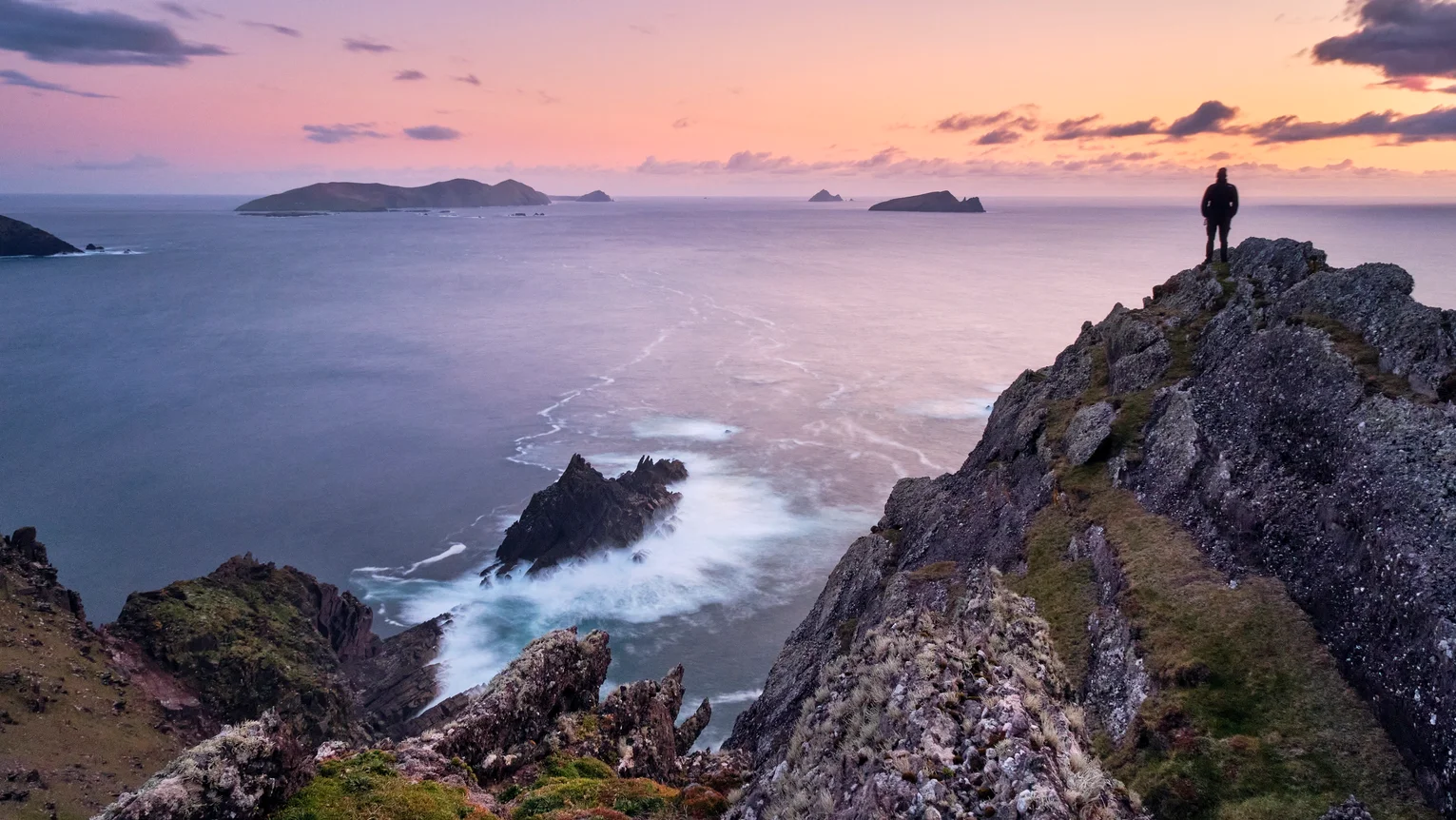 A person standing on a cliff overlooking a body of water