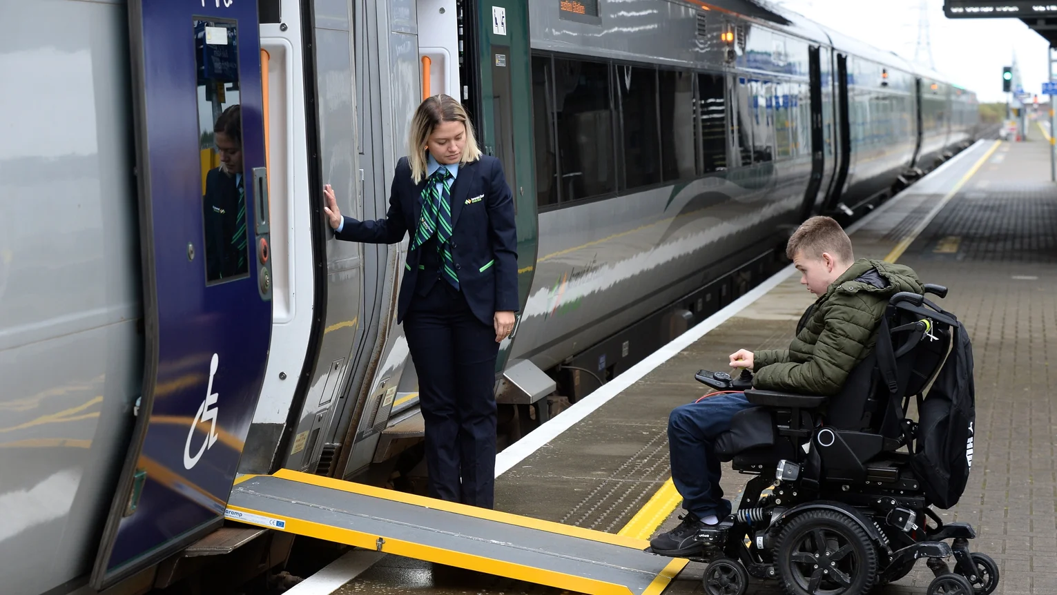 A woman helping a person in a wheelchair board a train