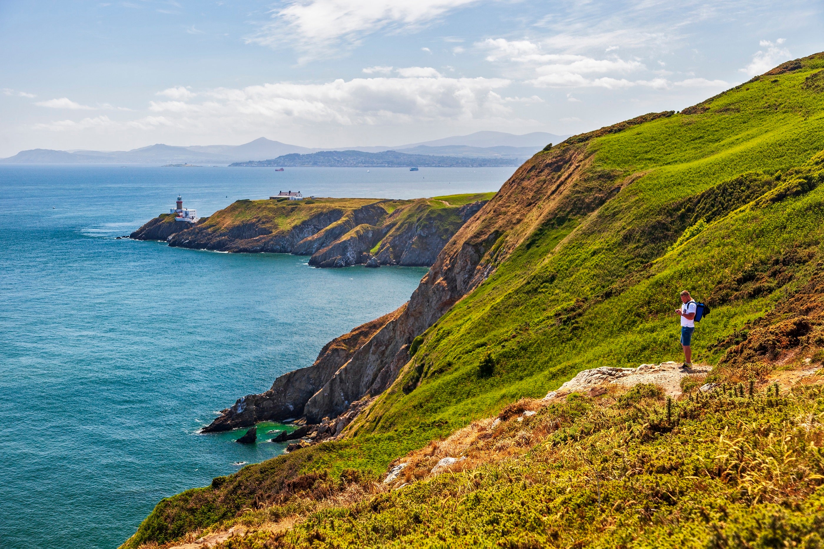 A person standing on a trail on  a hill overlooking the coast