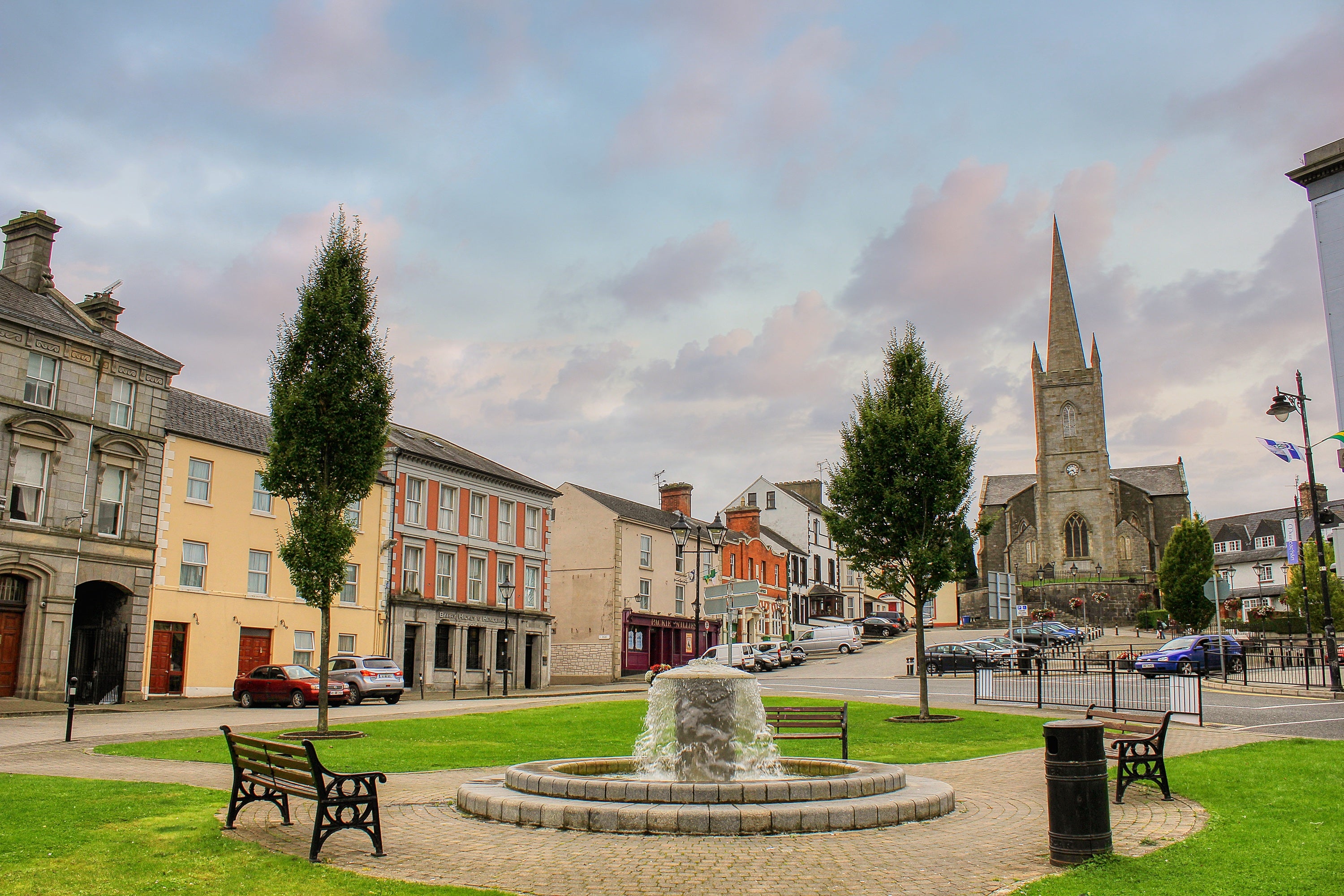 A fountain in a town centre with trees and buildings in the background