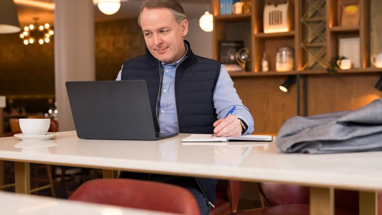Smartly dressed man working on a laptop in a hotel lobby.