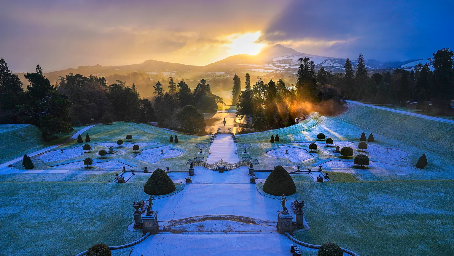 A garden with a path and trees and a snowy mountain