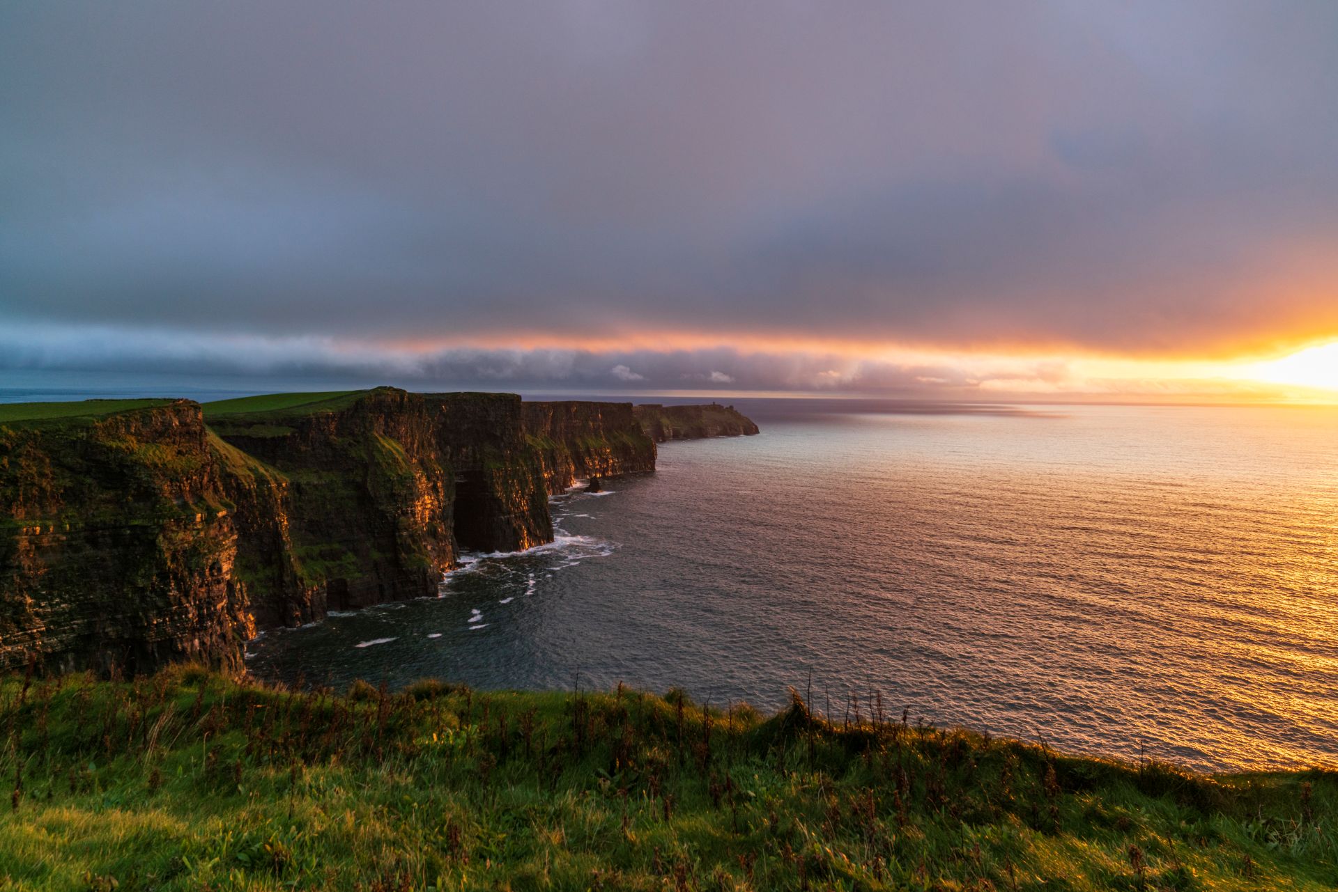 Sunset light over the Cliffs of Moher in Co. Clare, with rugged sea cliffs overlooking the Atlantic Ocean beneath dramatic clouds.