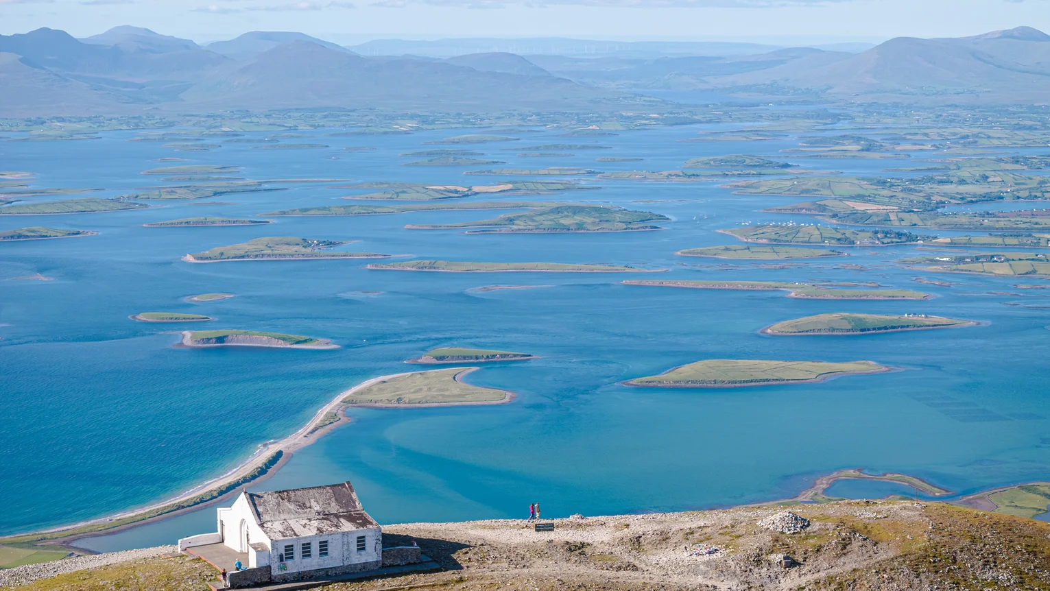 A house on a hill with water and mountains in the background