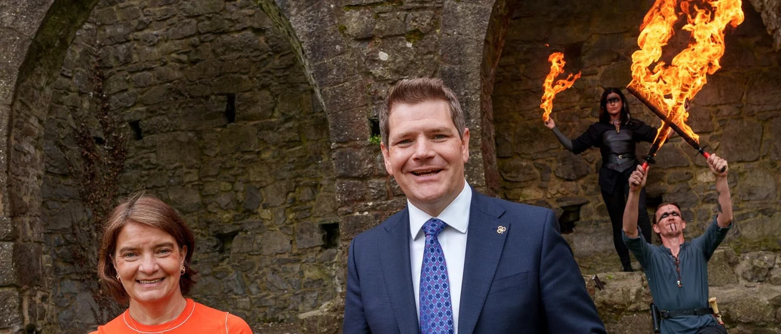 A man in a suit and tie smiling with a woman in the background