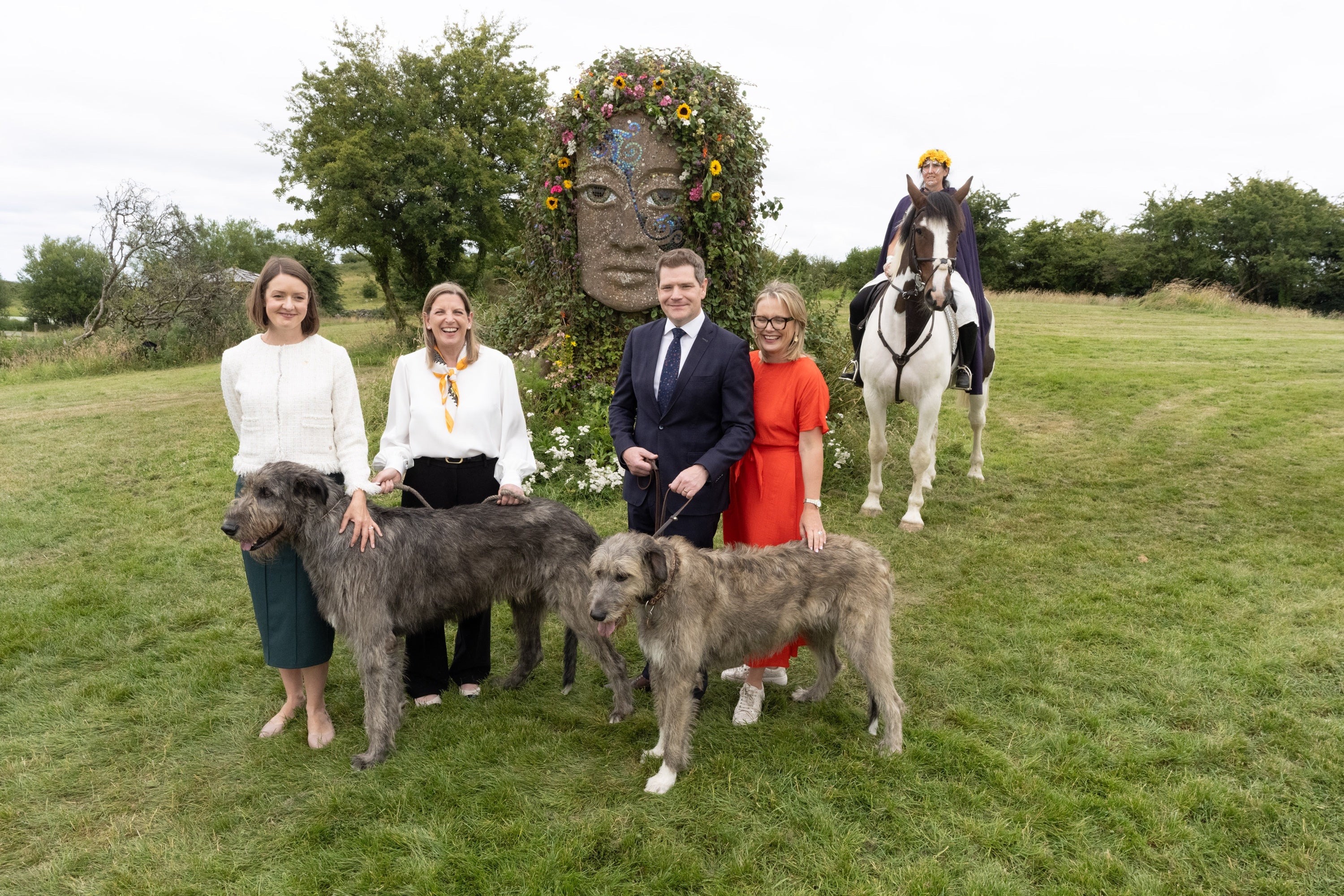 A group of people posing with dogs and horses in a grassy field
