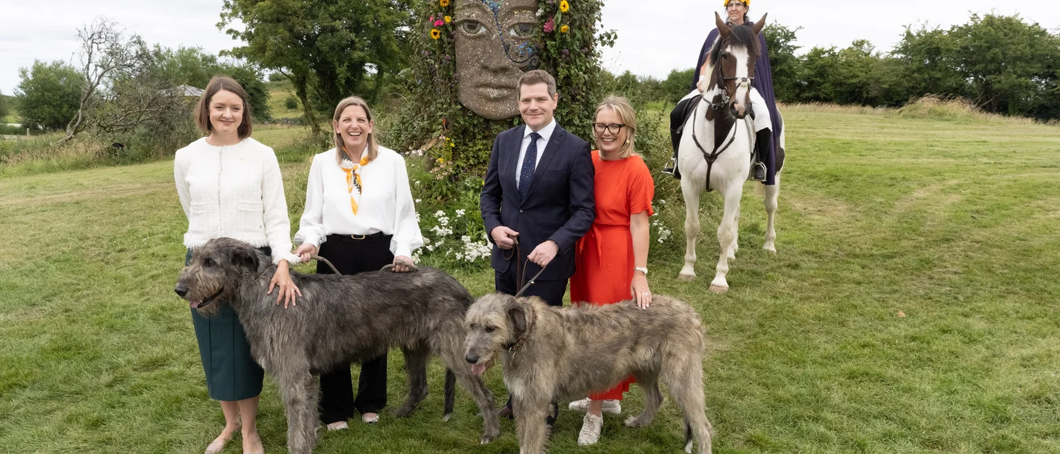 A group of people posing with dogs and horses in a grassy field