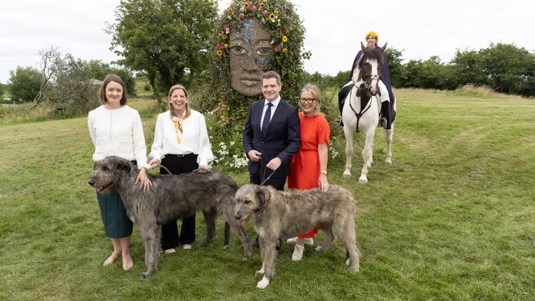 A group of people posing with dogs and horses in a grassy field